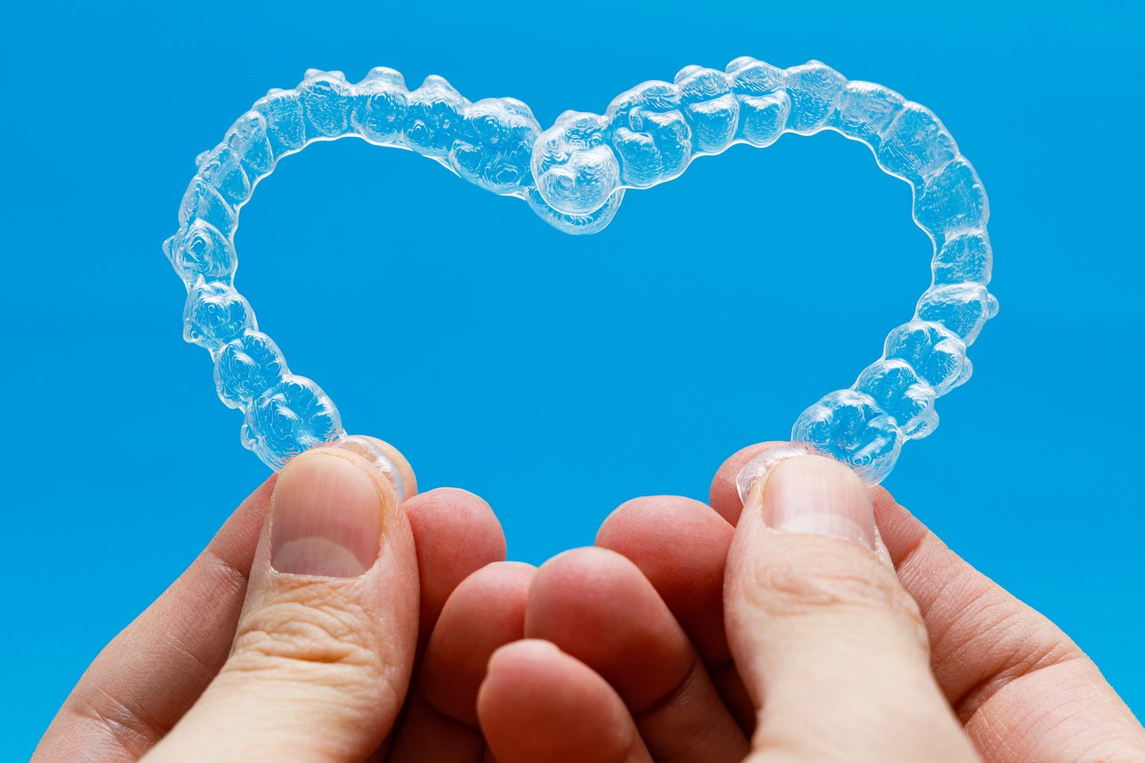 Hands Holding Dental Aligners in Heart Shape on Blue Background