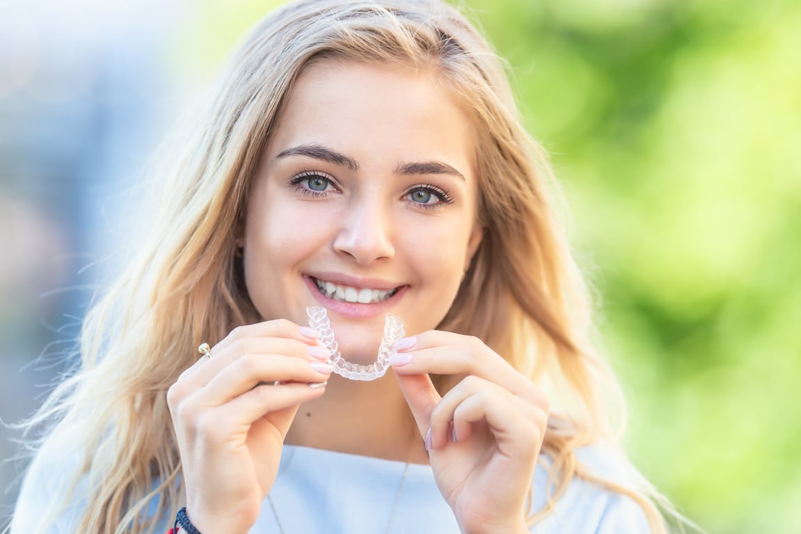 Invisalign orthodontics concept - Young attractive woman holding - using invisible braces or trainer.